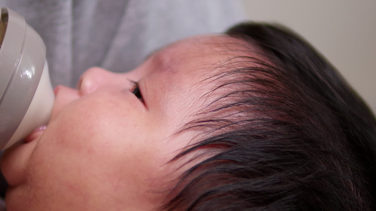 Pacifying a crying newborn child and feeding her baby with some formula milk in a feeding bottle.