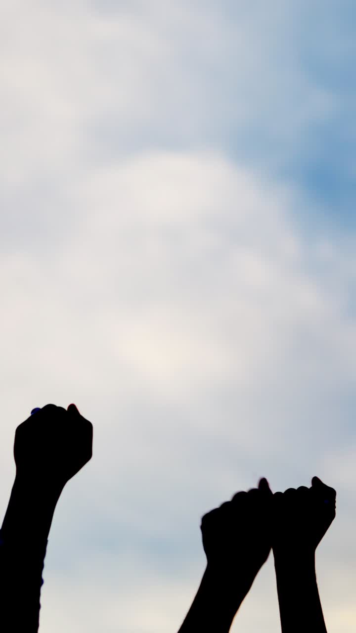 Silhouette on sky of hands of people waving in the air