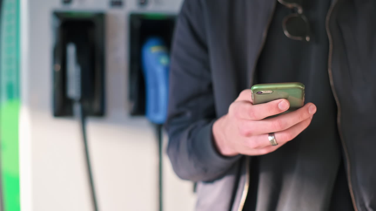 Hombre usando un smartphone cerca de un cargador de coche eléctrico