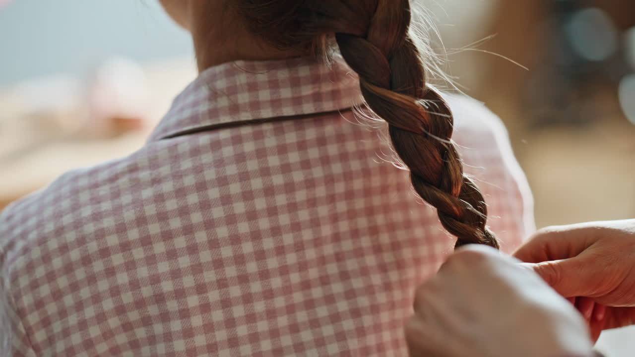 Primo piano delle mani che intrecciano i capelli di un bambino a casa. Donna irriconoscibile che fa un'acconciatura.