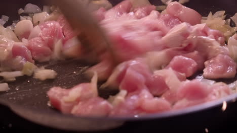 close-up: chicken and onions stirred in hot saucepan with wooden fork