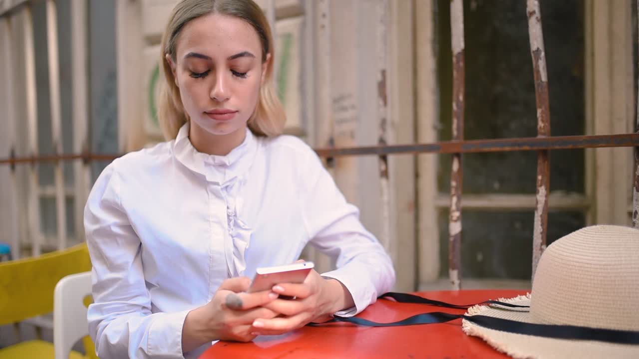 Slow Motion:Attractive young beautiful girl uses smart phone while sitting at a cafe outside