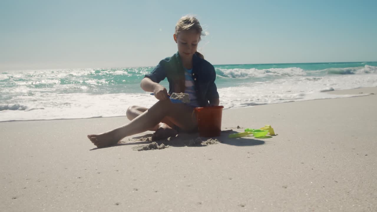 어린 소녀 가 모래 에 앉아서 놀고 있다