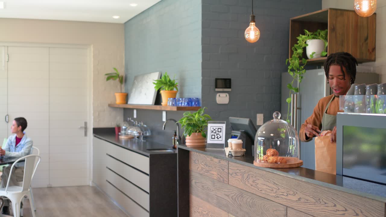 Barista afro-americano ensacando croissants enquanto cliente entra no café para fazer um pedido, espaço para texto