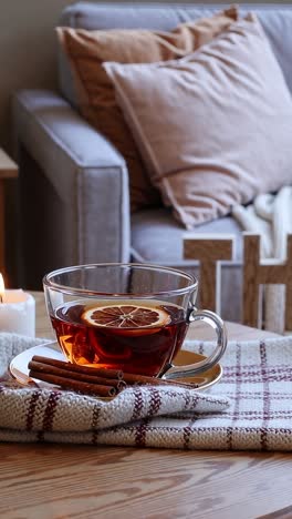 glass cup of hot tea with lemon and cinnamon sticks sits on a wooden table in a cozy living room, creating a warm and inviting atmosphere