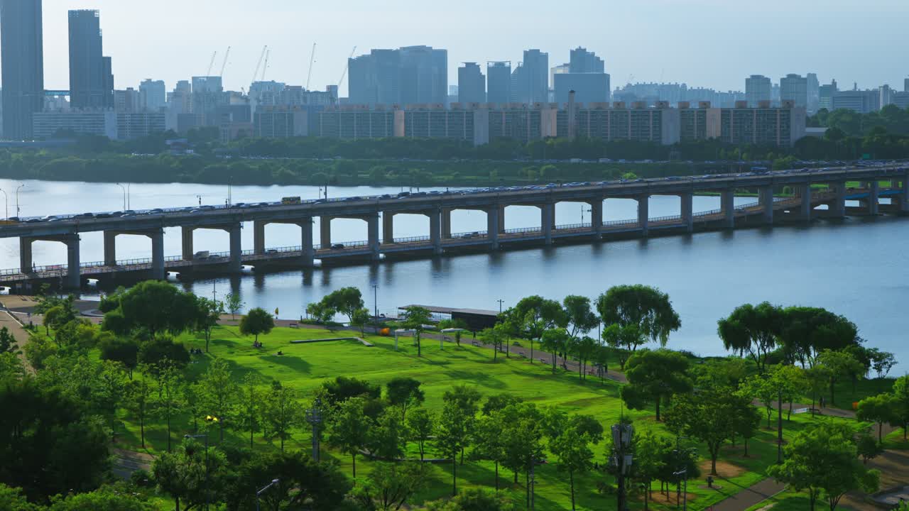 Real-time aerial view of vivid green Hangang Park with car traffic on the Banpo Bridge and the Seoul city skyline in the background