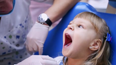 Little child in stomatology chair opens her mouth wide and shows her teeth to the doctor - close up video.