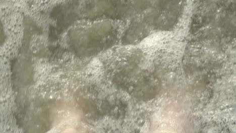 waves rushing over bare feet on sandy beach in slow motion