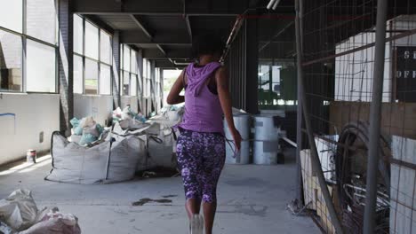 Mujer-Afroamericana-Vistiendo-Ropa-Deportiva-Corriendo-Por-Un-Edificio-Urbano-Vacío