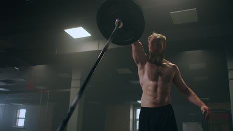 a male athlete lifts a weight bar with one hand in slow motion. strength training for a boxer. the man is sweating working out in the gym practicing the force of the blow with his hand