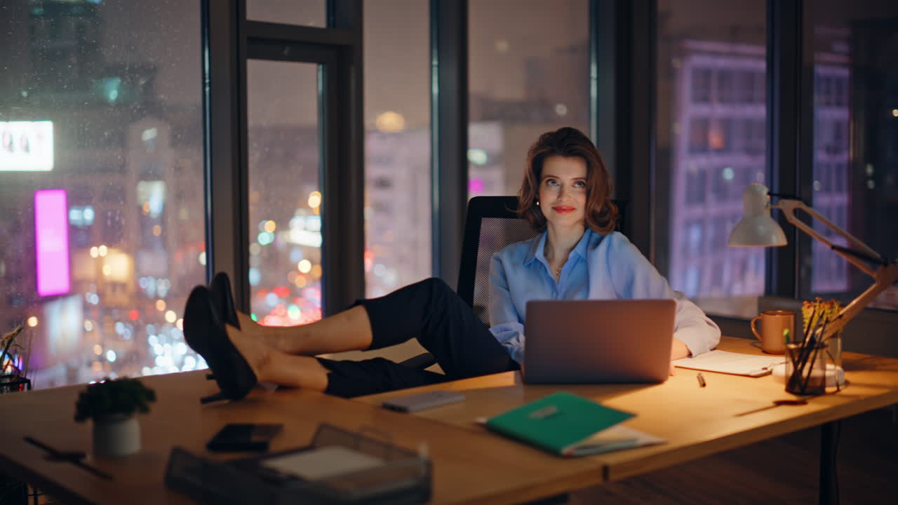 Successful lady browsing laptop at night workspace in lamp light. Smiling woman