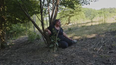 distressed woman resting under a tree in a forest