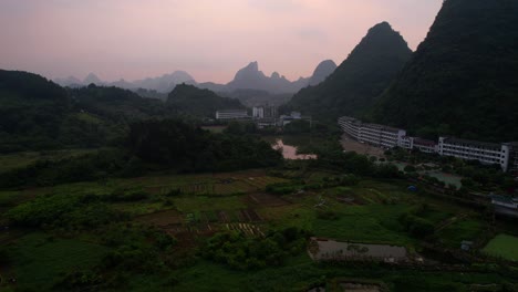 Aerial-shot-moving-downwards,-showing-farm-fields-surrounded-by-Guilin-mountains-at-sunrise