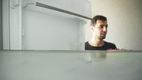 Young-man-opens-the-fridge-and-takes-out-the-cake-decorated-with-raspberries