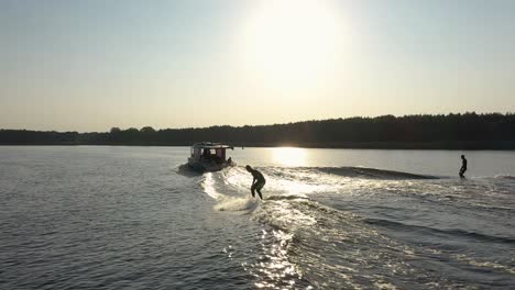 two surfers on surfboard surfing waves behind boat in sunset 005