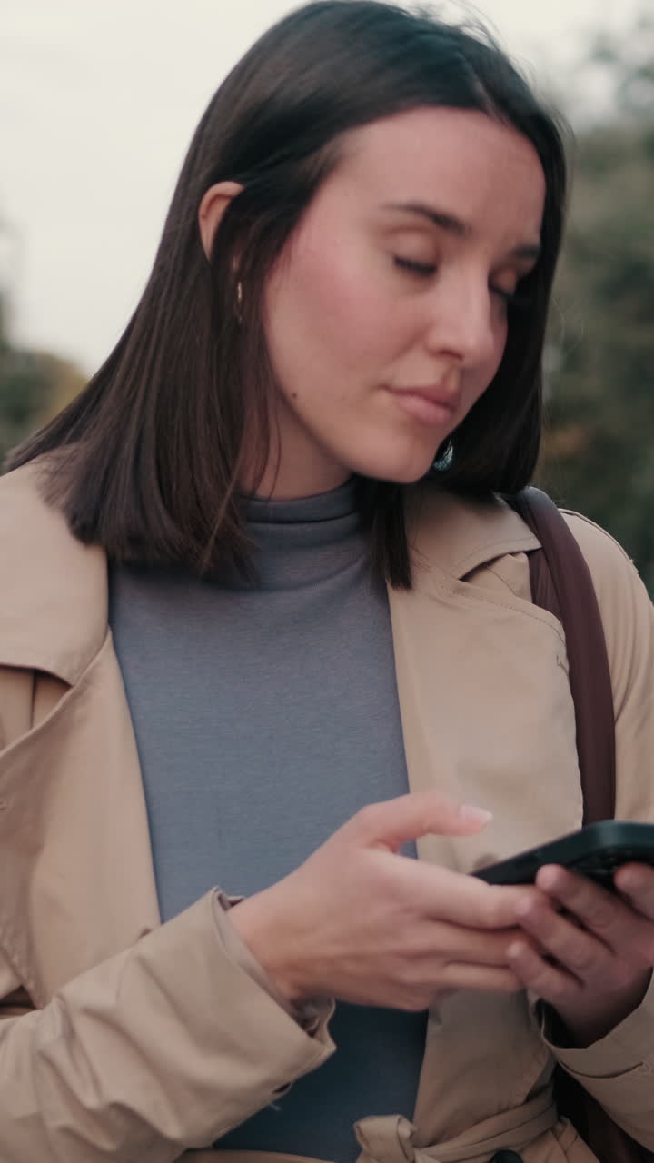 Giovane donna che usa lo smartphone all'aperto in un trench