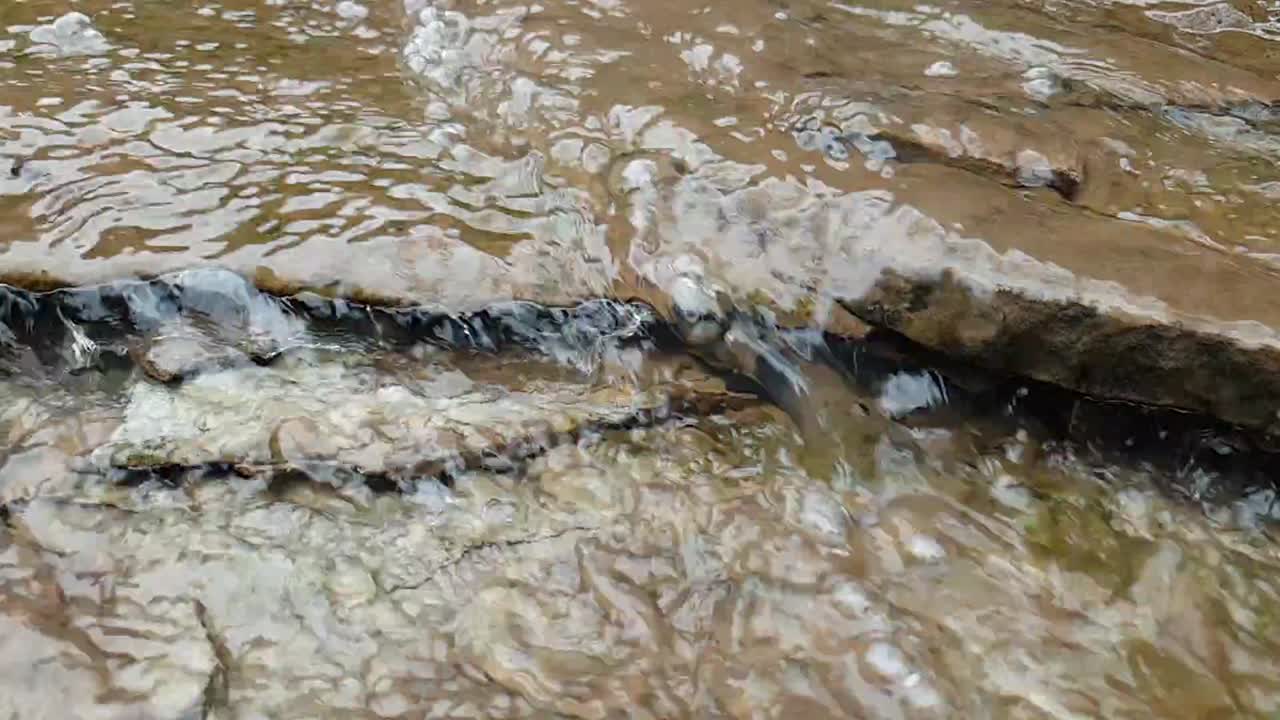 agua que fluye de un arroyo de agua de manantial de montaña que corre por enormes losas de piedra arenisca de roca con musgo verde, agua potable cristalina, meditación tranquila y pacífica en cámara lenta