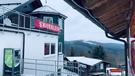 german ski rental house with information sign with hills and small huts in the background