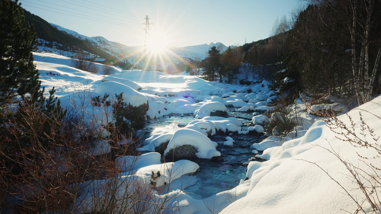 Bright sun rays illuminate snowy river winding through quiet mountain valley