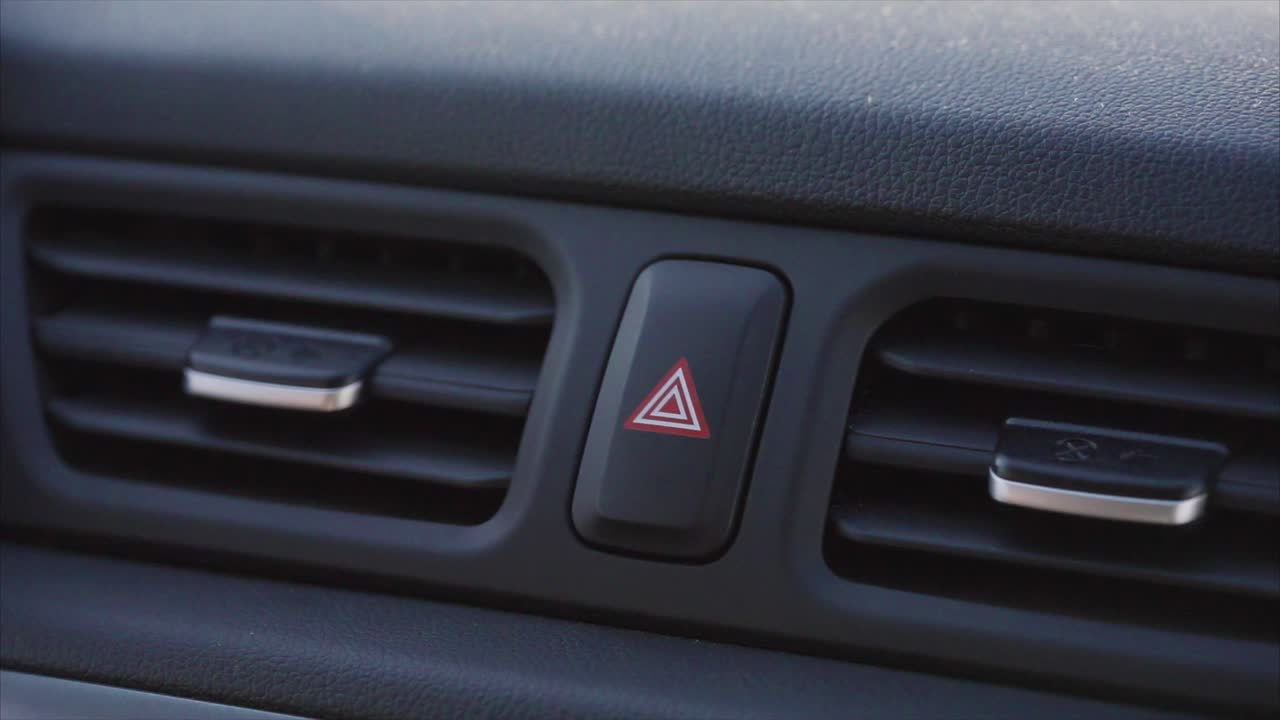 presionando con el dedo el botón de las luces de peligro del coche