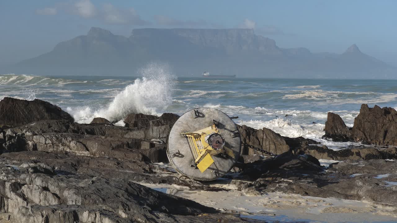 A weather buoy rests on Blouberg Beach rocks with Table Mountain in the background after a storm