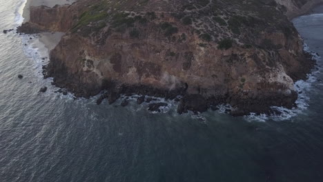 Aerial-Slide-Dolly-right-with-view-on-Malibu-Coastline-in-California,-Waves-Crashing-at-Sunset