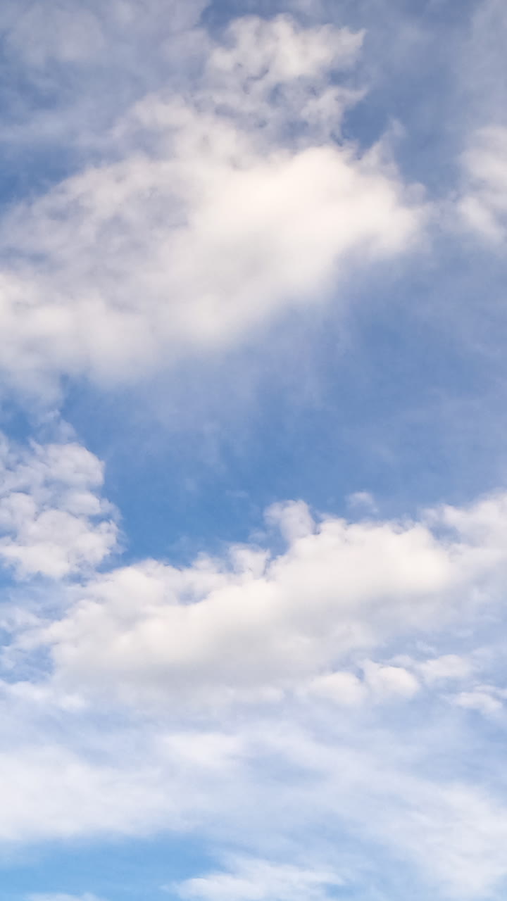 Light white cloudscape in the beautiful blue sky. Soft clouds floating in the atmosphere. Low angle view. Timelapse. Vertical video
