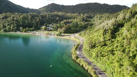 Lakeside-holiday-campground,-blue-lake,-palm-forest-road-and-tourist-on-paddle-bord-4k-drone-shot-in-New-Zealand