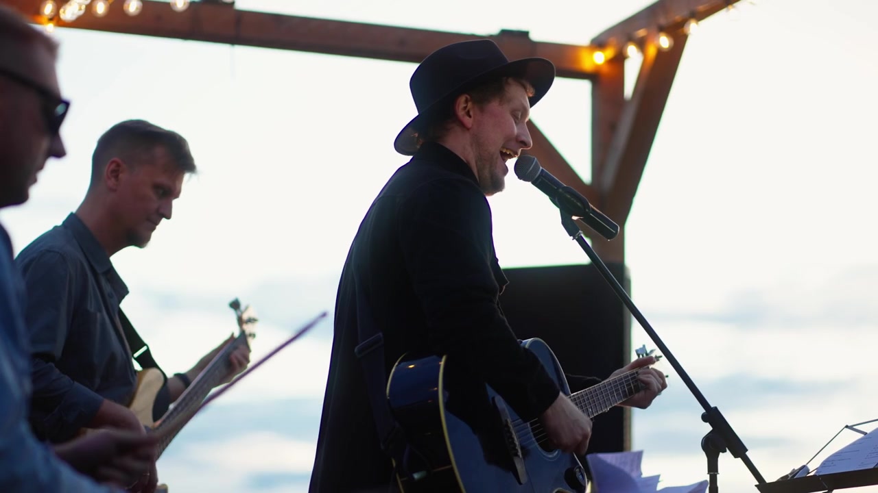 Liveband spiller akustisk musik på en udendørs scene ved solnedgang