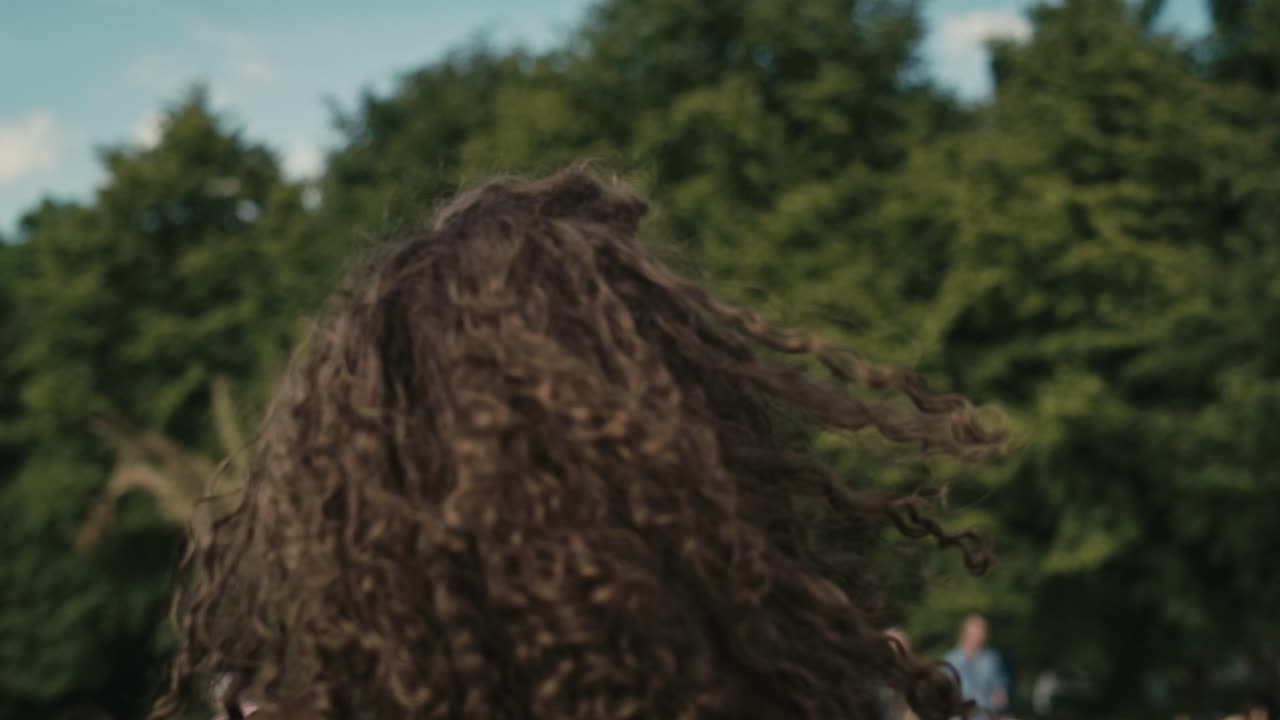 Camera tracking smiling young caucasian woman with curly hair dancing at music festival.