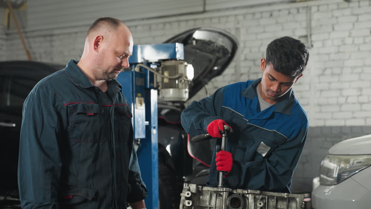 ingenieros de automóviles en un taller mecánico, uno con guantes rojos apretando una nuez en el motor del automóvil mientras un colega observa, el fondo presenta vehículos, herramientas y equipos mecánicos