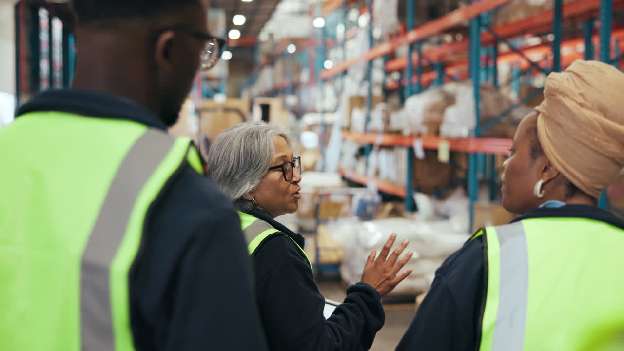 Three Workers in Safety Vests Talking in a Large Warehouse