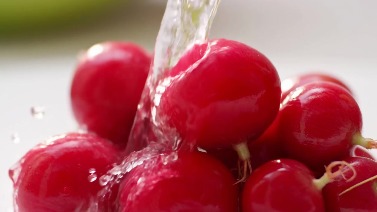 Urutan awal tampilan jarak dekat gugusan ceri merah cerah yang terpusat di bingkai saat air jernih mengalir di atas buah yang mengkilap, menciptakan percikan, tetesan, dan sebuah...