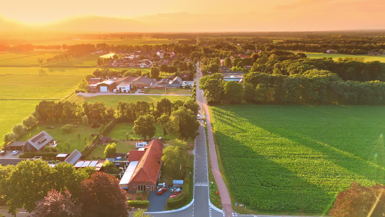 Stunning warm light of setting sun colors the scenery of the green countryside. Drone footage above the straight road crossing the rural area. The Netherlands