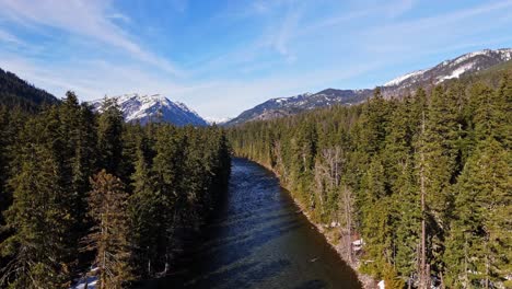 ascending shot of scenic view of river and evergreen forest with mountains in the background in cle elum on a clear day in washington state