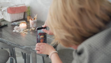 close up backview of young adult capturing cozy candlelight setting with smartphone held upside down, adjusting angle to frame basket, seashells, and decor items on wooden table