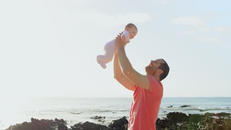 side view of mid adult caucasian father holding baby in the air at beach on a sunny day 4k