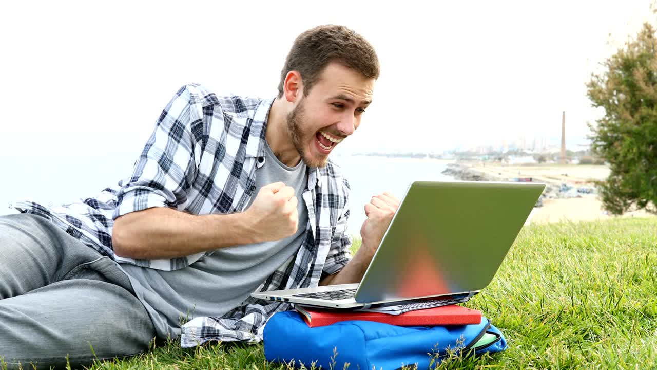 estudiante emocionado usando una computadora portátil en el césped