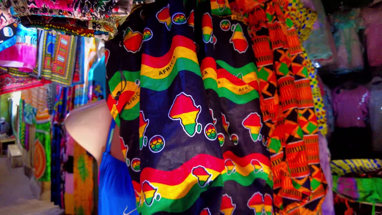 African clothing with continent pattern and rasta red yellow green stripes displayed at Serekunda Market, with vibrant fabrics