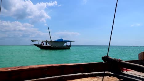 traditional african wooden boat with a sailor seen from another boat navigating in the turquoise waters of zanzibar, tanzania