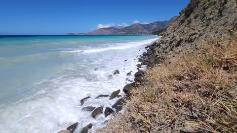 White-Waves-Carving-Rocky-Mediterranean-Beach,-Lush-Green-Herbariums-Adorn-the-Shoreline-in-a-Coastal-Wilderness-Scene