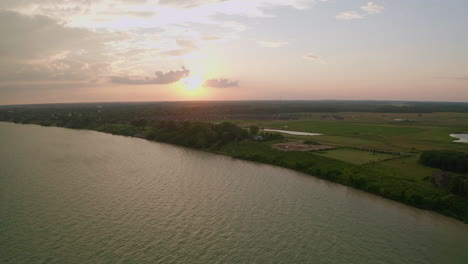 drone flies out over lake erie facing sunset, cottages, suburbs and field in the distance