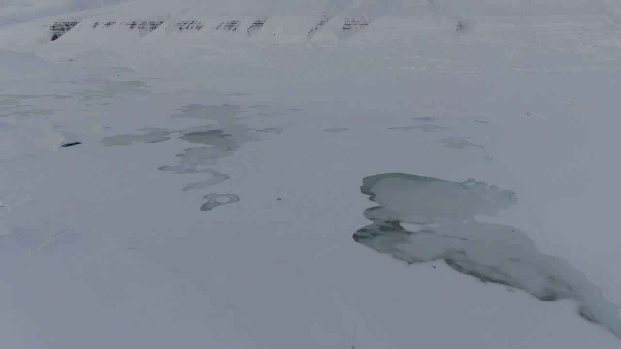 vista de avión no tripulado en svalbard volando sobre montañas blancas nevadas con lagos congelados en noruega en un día nublado