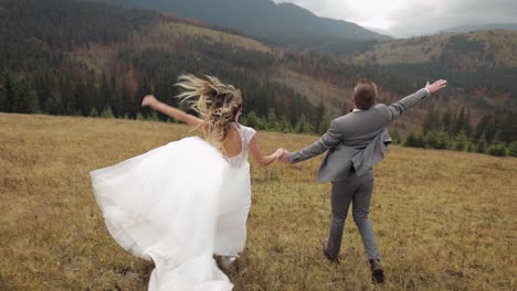 happy wedding couple running in mountain field