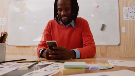 Animation-Der-Datenverarbeitung-über-Einem-Afroamerikanischen-Mann,-Der-Lächelt,-Während-Er-Im-Büro-Sein-Smartphone-Benutzt