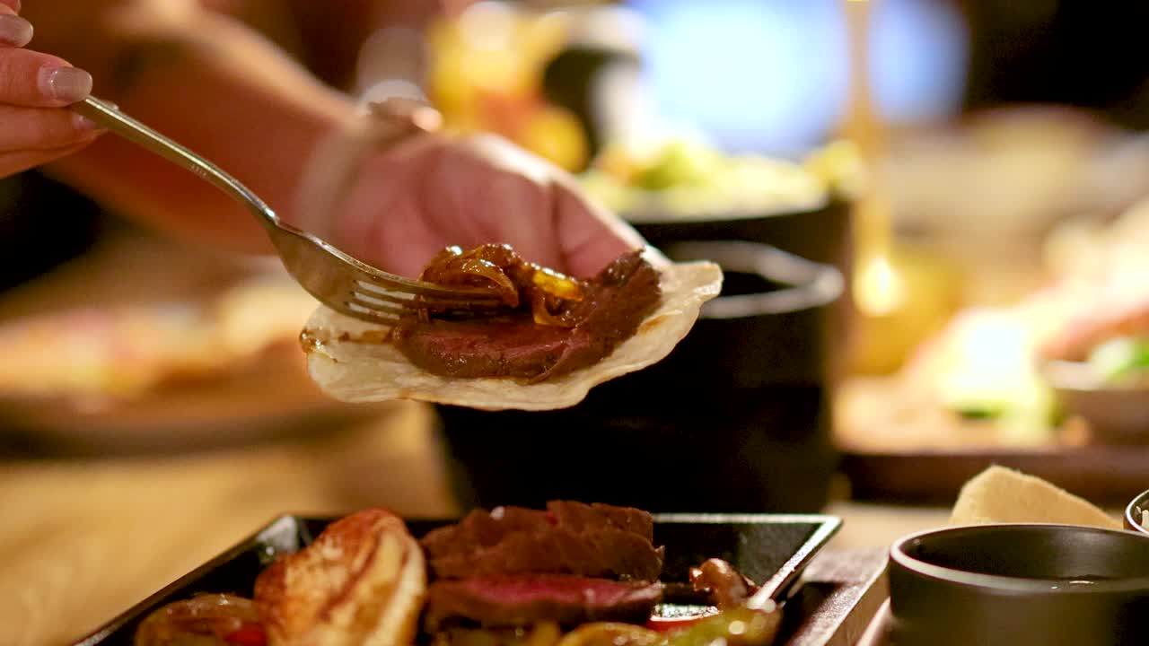 Hand adds grilled beef and caramelized onions to taco shell under warm, ambient restaurant lighting