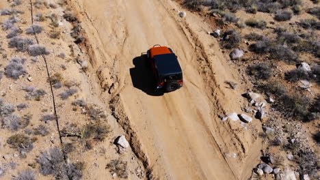 Antena-De-Un-Vehículo-Todoterreno-Naranja-Que-Conduce-Por-Un-Camino-De-Tierra-A-Través-De-Las-Montañas-Del-Desierto---Vista-Superior-Y-Lateral-Del-Vehículo