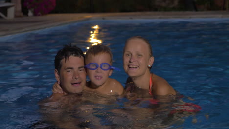 Familia-Feliz-Con-Niño-En-La-Piscina-Por-La-Noche