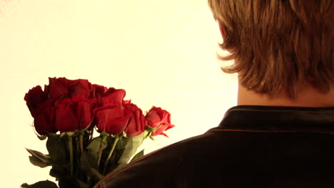 a man holds flowers in his hand and a cleaver  behind his back