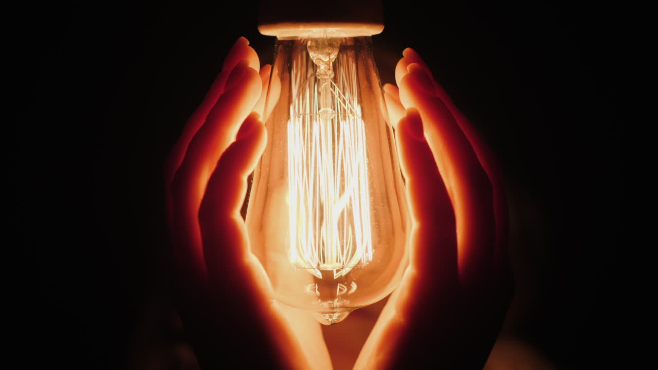 사람의 뒷모습은 어둠 속에서 전구 근처에서 손을 따뜻하게 한다